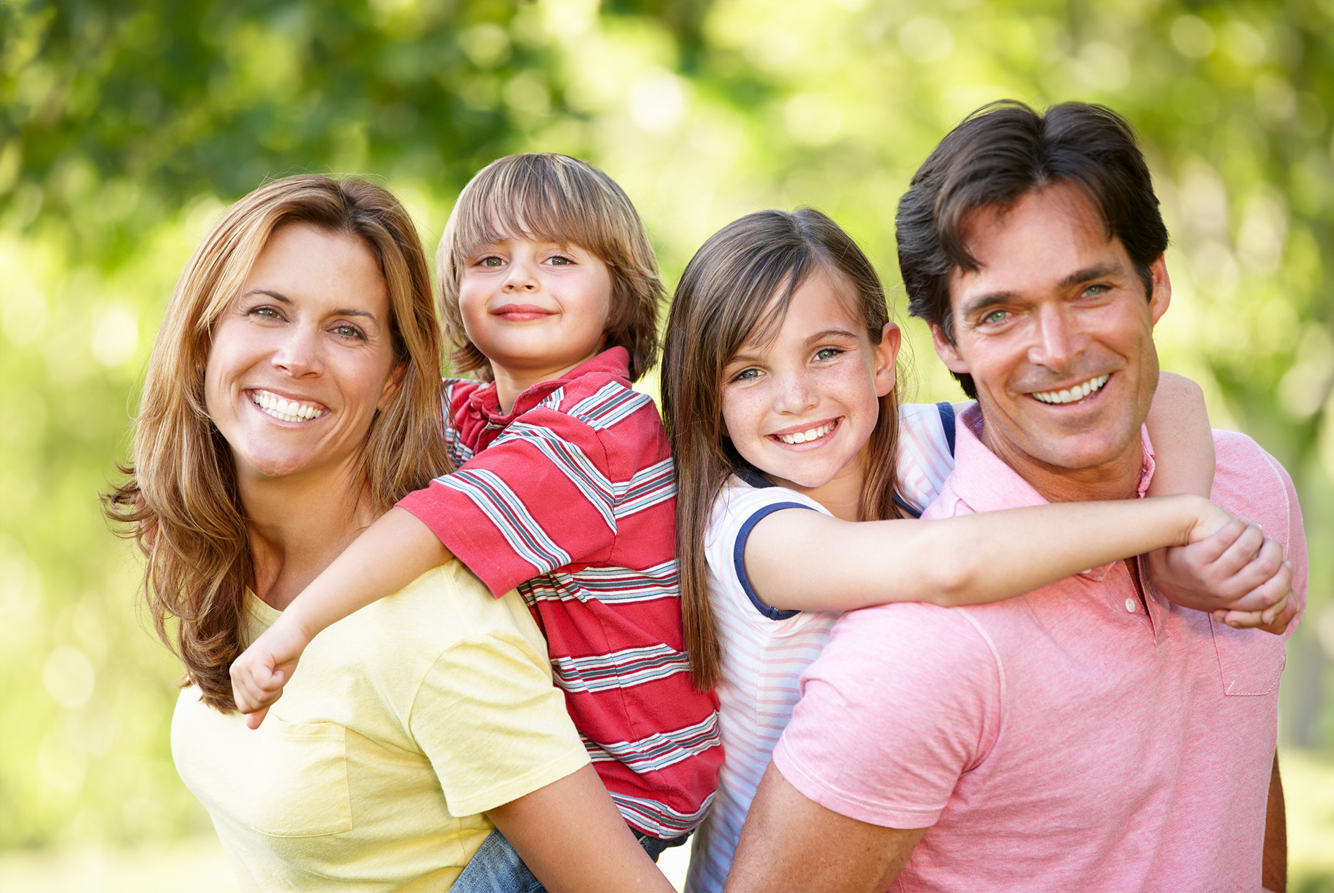 Family of four, including two adults and two children, posing for a photo outdoors with trees in the background.