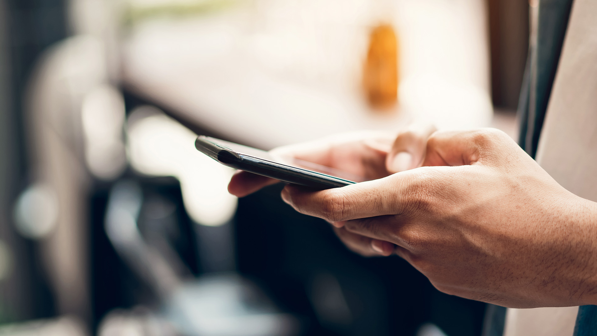 This is a photograph of a person using a smartphone, with the phone held in their hand and the screen visible. The individual appears to be standing outdoors, as suggested by the blurred background that includes what seems like a street scene.