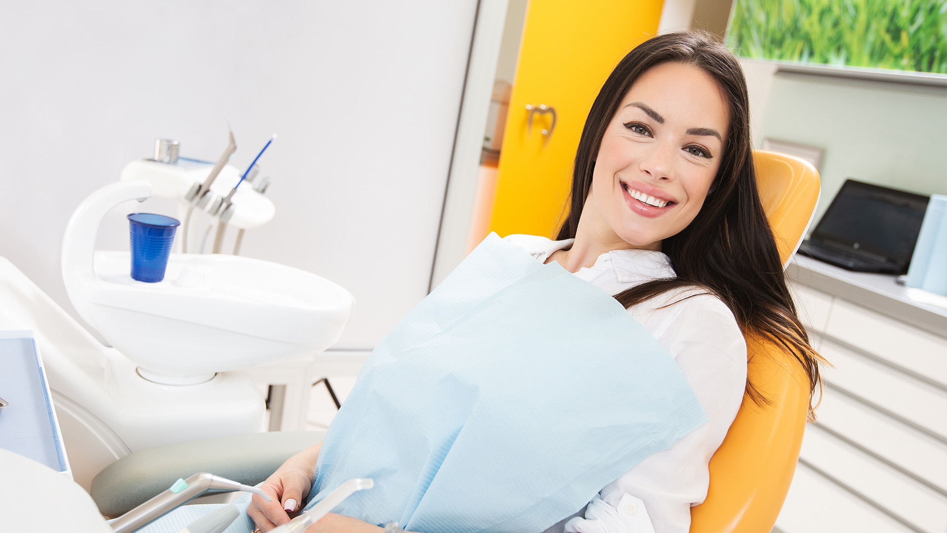 A woman sitting in a dental chair, smiling at the camera, with dental tools and equipment around her.