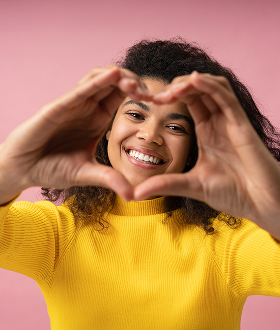 A young woman with a radiant smile is making a heart shape with her hands, expressing joy and love.