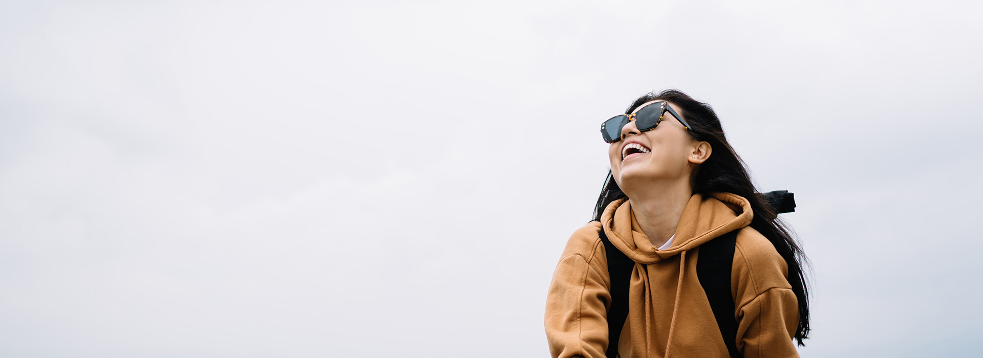 A person with a backpack and sunglasses, standing outdoors against a cloudy sky.