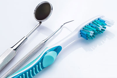 The image shows a collection of dental tools, including a toothbrush with blue bristles, a pair of tweezers, and other instruments commonly used in dental care.