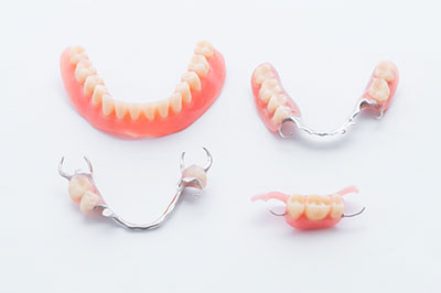 The image shows three pairs of dentures with a pinkish hue, displayed against a white background.