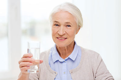 An elderly woman holding a glass of water and smiling.