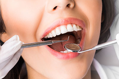 The image displays a woman with open mouth, receiving dental care as evidenced by the presence of dental tools and a dental hygienist s hand in her mouth.