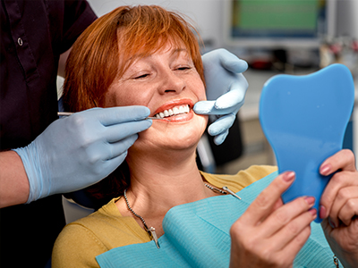 The image shows a woman in a dental chair, receiving dental care with a smile on her face.