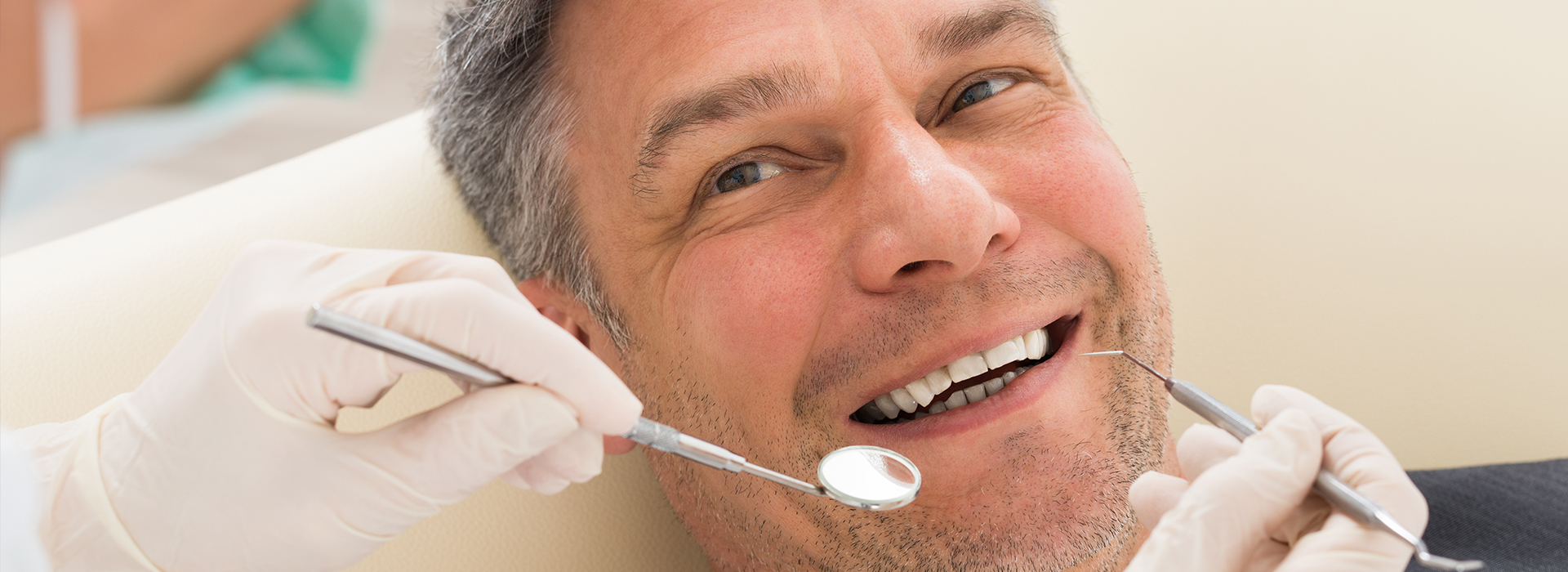 The image shows a man sitting in a dental chair, receiving dental treatment, with a smile on his face.