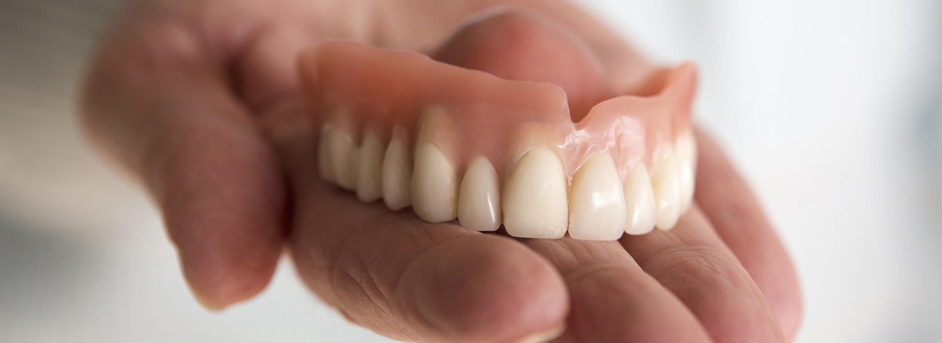 A person holding a set of dentures, showcasing the upper and lower arches.