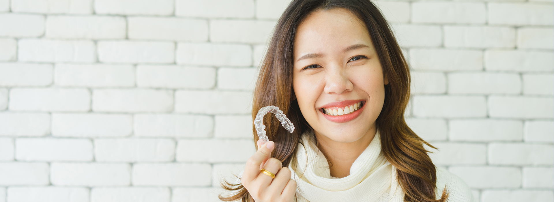 A woman smiling and holding a ring in front of her, against a blurred background.