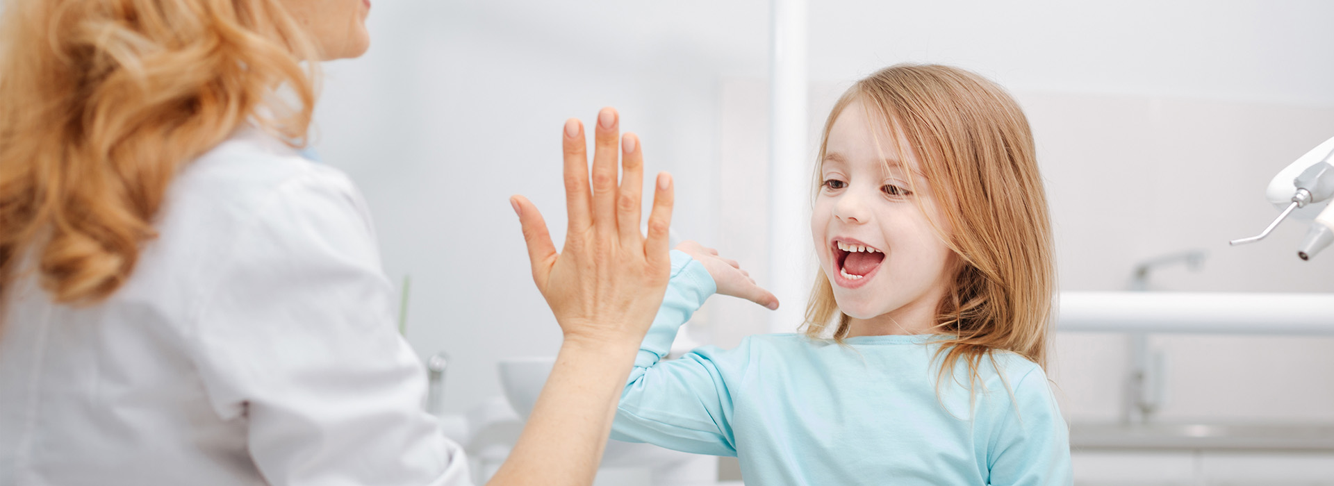 A woman and a young girl in a dental office, with the woman holding up her hand to the girl s face, both smiling.