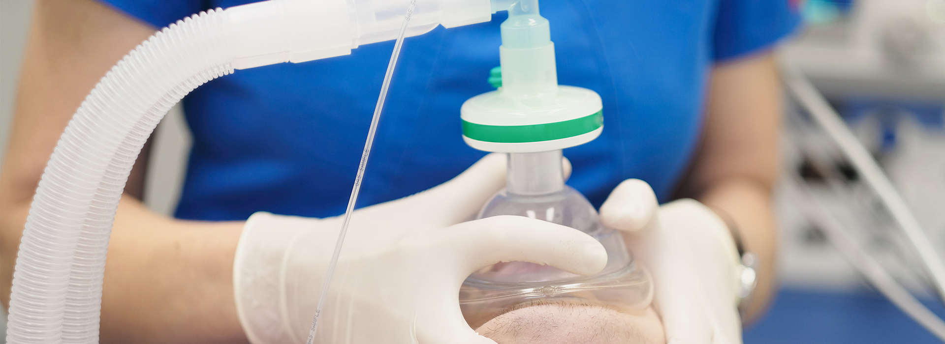 A person wearing gloves is holding a clear plastic container with a green cap, possibly containing medical equipment or supplies.