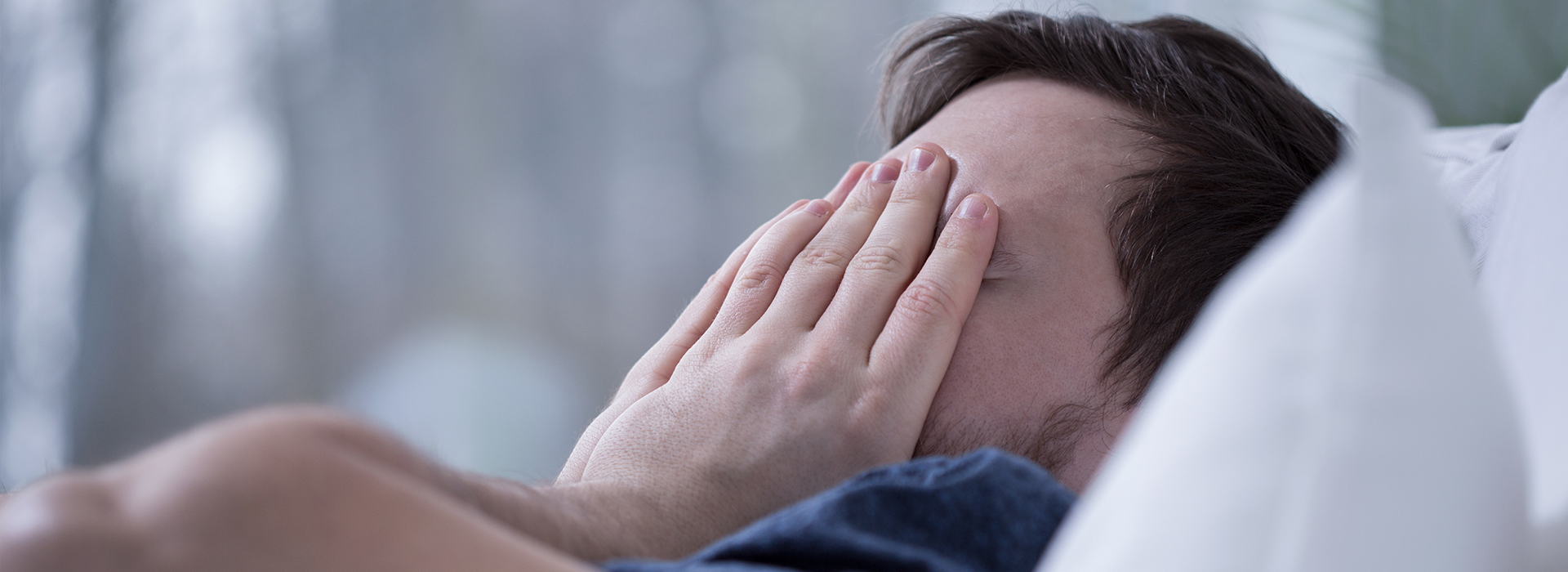 A person is lying down in bed, with their face hidden behind their hand.