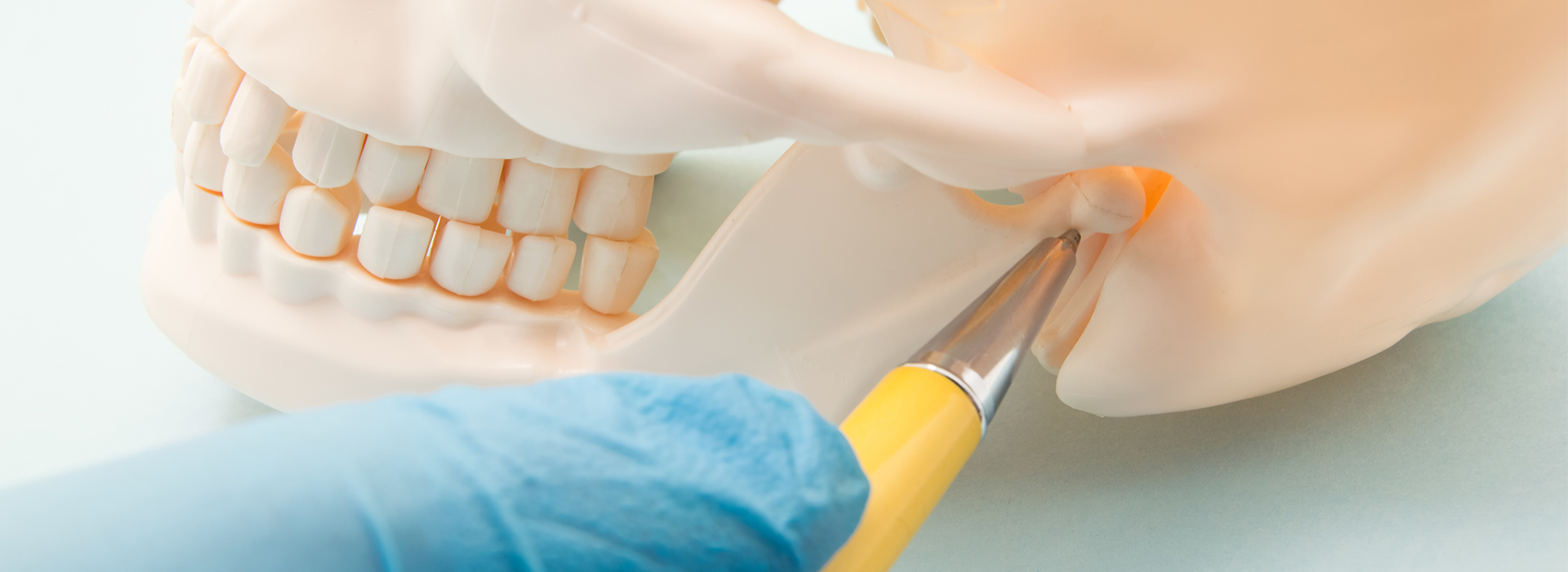 The image features a close-up of a dental procedure with a hand holding a small instrument, working on a model or dummy head in a clinical setting.