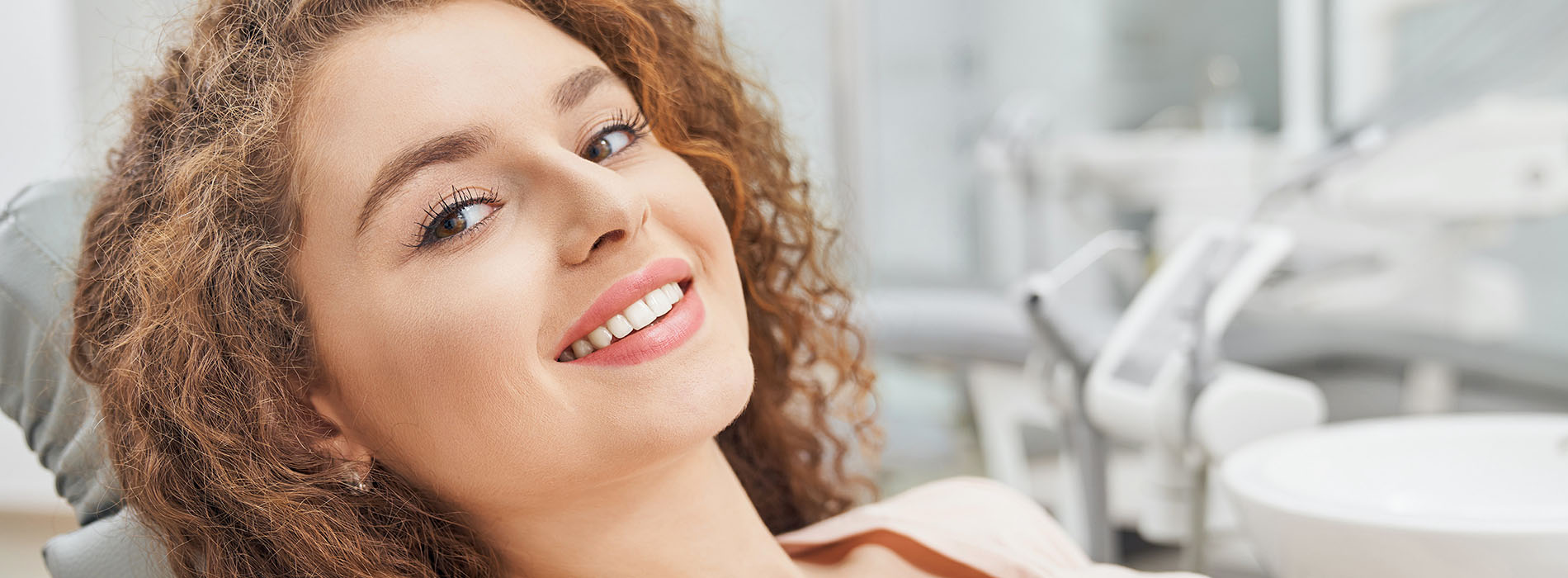 A woman sitting in a dental chair, smiling at the camera.