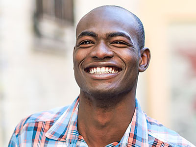 The image features a smiling man with short hair, wearing a blue and white plaid shirt.