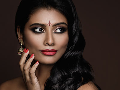 A woman with dark hair and makeup, posing for a portrait with her hand near her face.