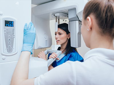 A woman in a blue coat and gloves is assisting another individual with a large, modern 3D scanner machine.