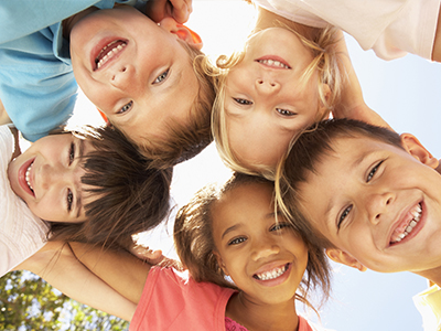 A group of children with varying expressions, gathered in a circle and smiling at the camera.