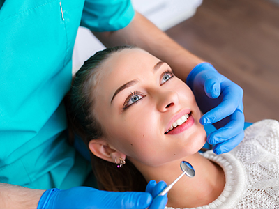 A dental hygienist is performing a teeth cleaning procedure on a patient, with the patient smiling and the hygienist focused on their work.