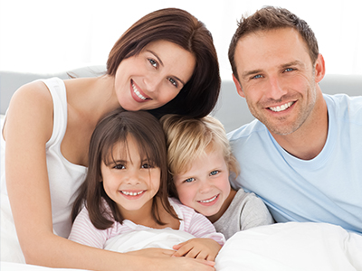 Family of five posing on bed with adult couple and three children.